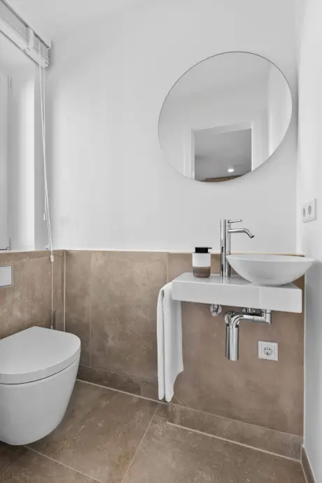 Modernes Badezimmer mit elegantem Waschbecken, Toilette, Spiegel und einem Handtuch.