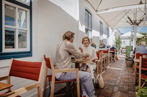 Ein Mann und eine Frau sitzen an einem Tisch im Freien vor dem Hotel Stadt Hamburg in Westerland / Sylt.