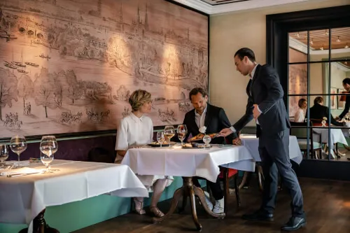 Ein Mann, der in einem Restaurant der 12.18. Hotel Stadt Hamburg GmbH eine Frau am Tisch bedient