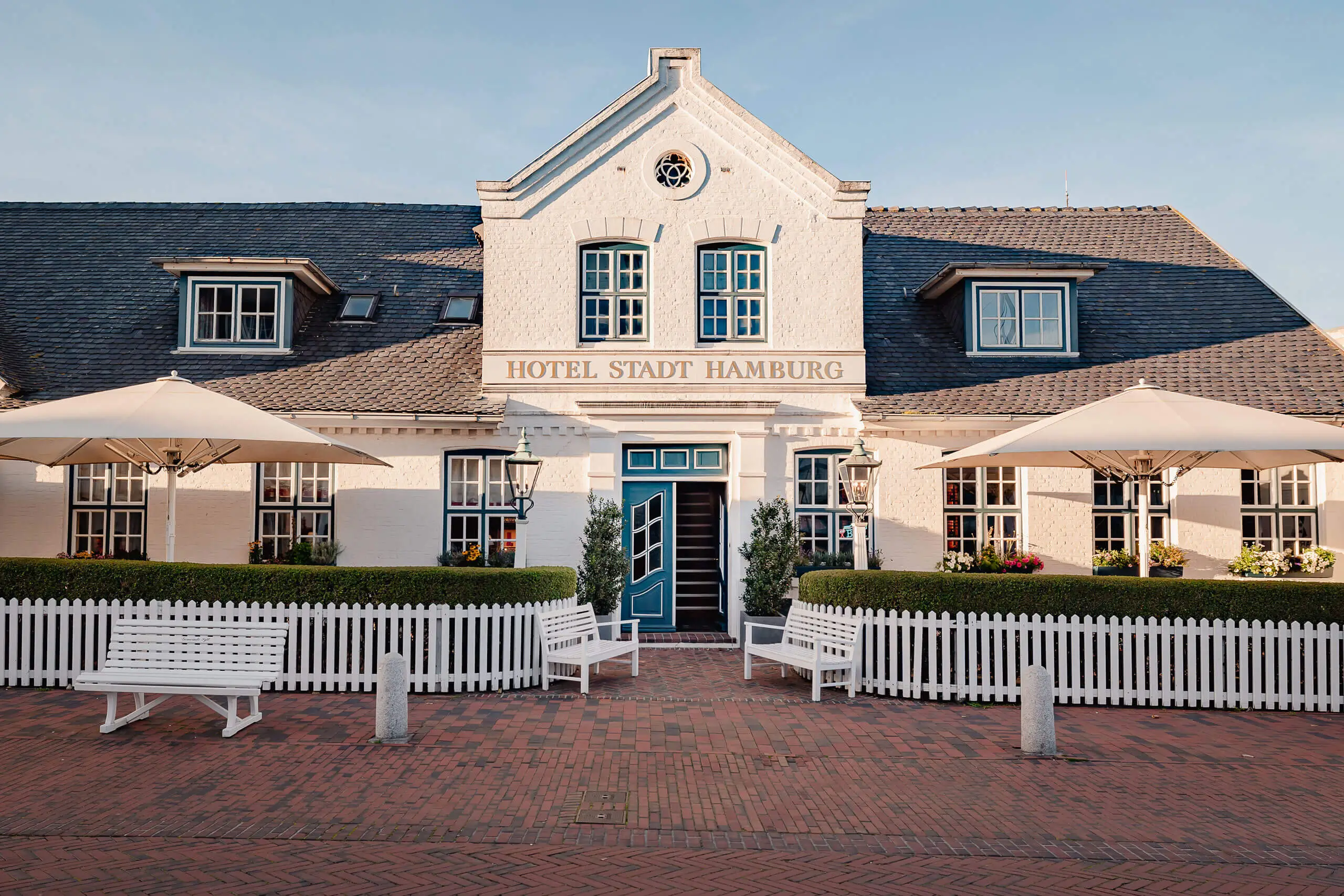 Fassade des Hotel Stadt Hamburg mit Außenbereich und farbenfrohen Sonnenschirmen.