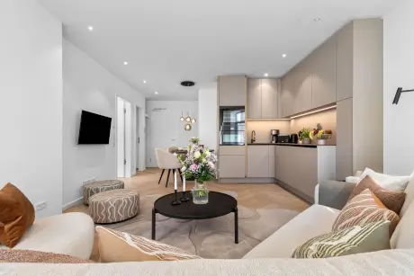 Innenansicht eines modernen Hotelzimmers mit Sofa, Küche und frischen Blumen.