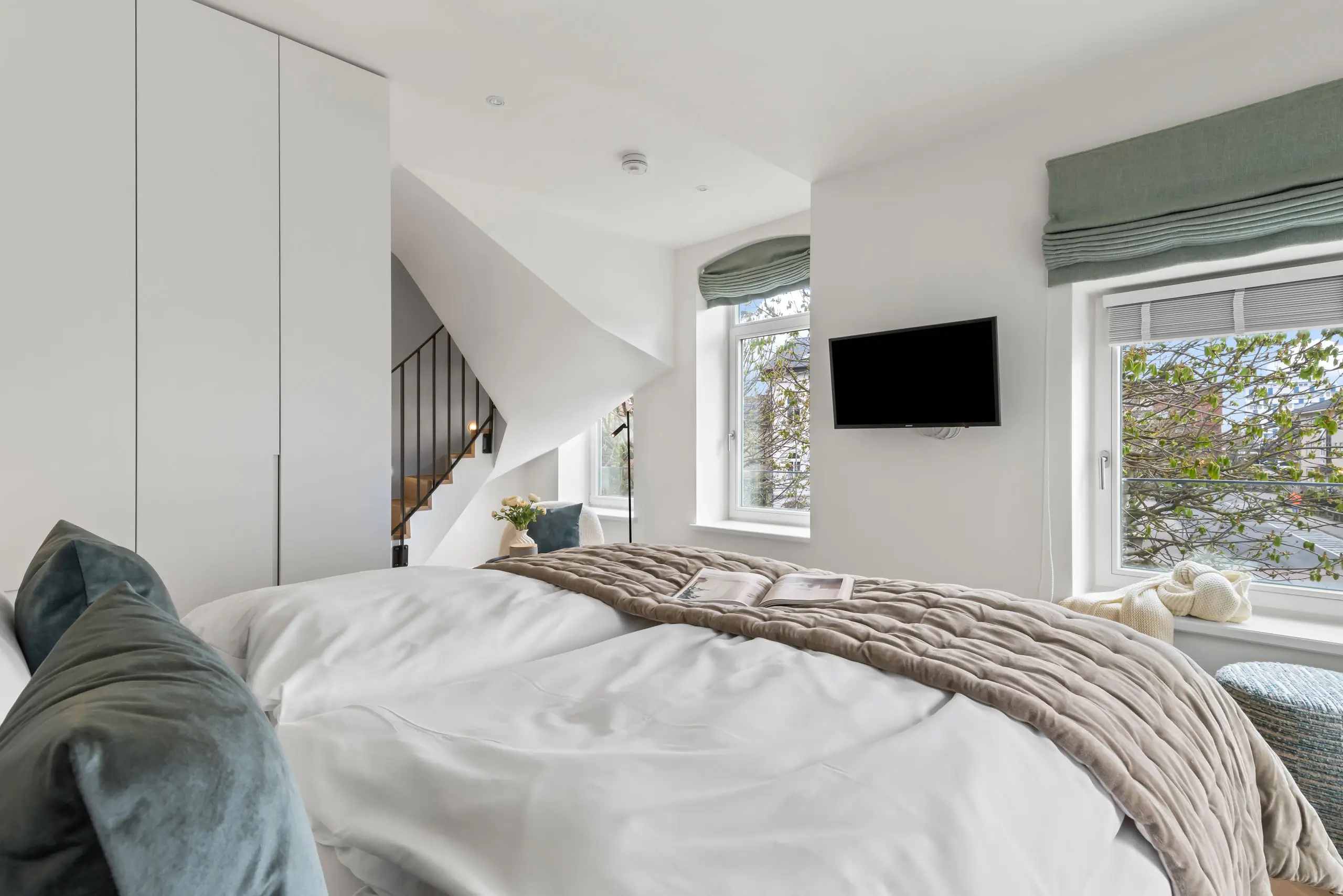 Helles Hotelzimmer mit einem bequemen Bett, Fernseher, Treppe und gemütlicher Atmosphäre.