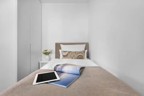 Behagliches Hotelzimmer mit Tablet, Magazin und Blumen auf dem Nachttisch.