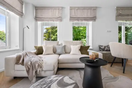 Modernes Wohnzimmer mit beigem Sofa, stilvollem Tisch, dekorativen Kissen und großen Fenstern.