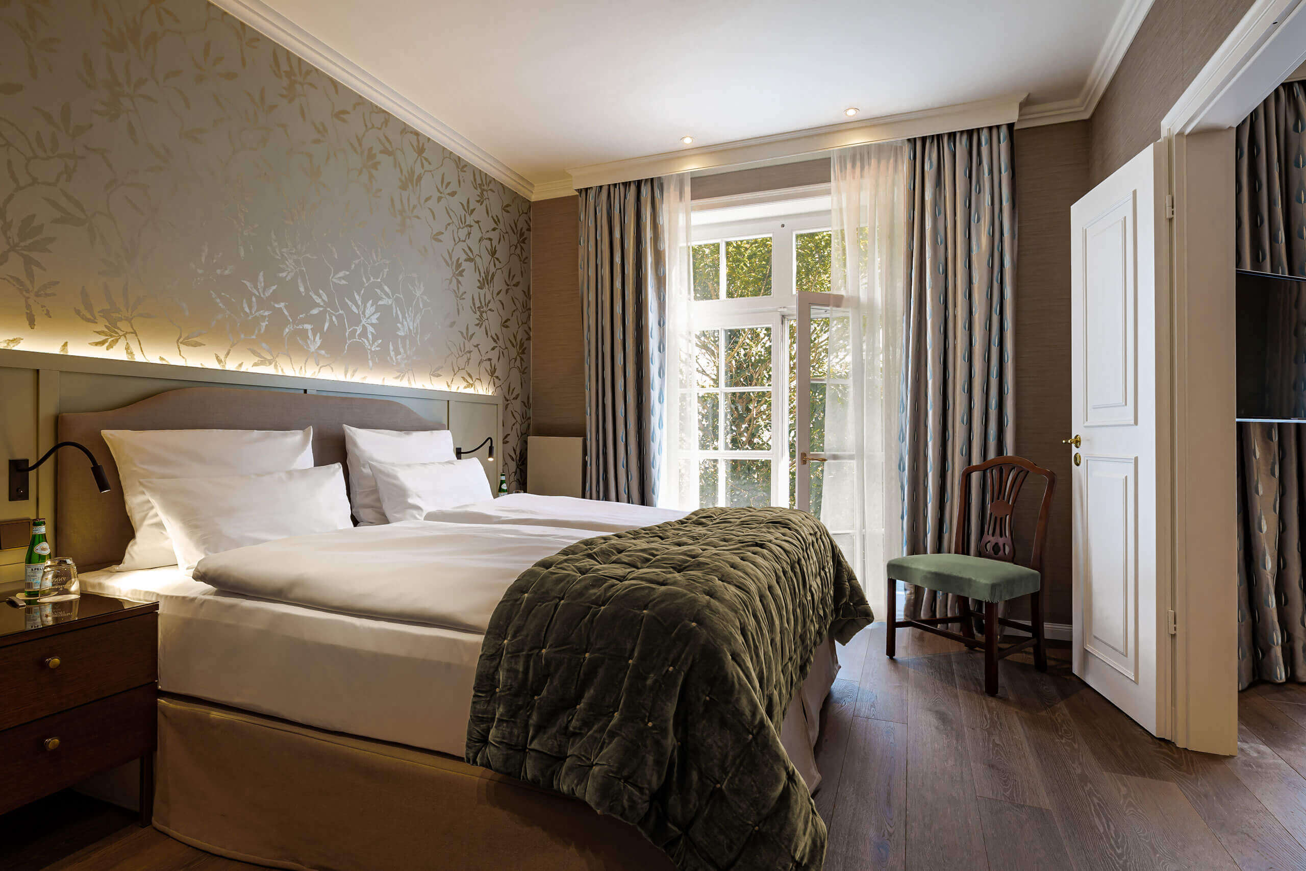 Ein Bett mit grüner Decke in einem Raum mit Tür und Fenstern. Luxuriös in Westerland, 45 Zimmer u